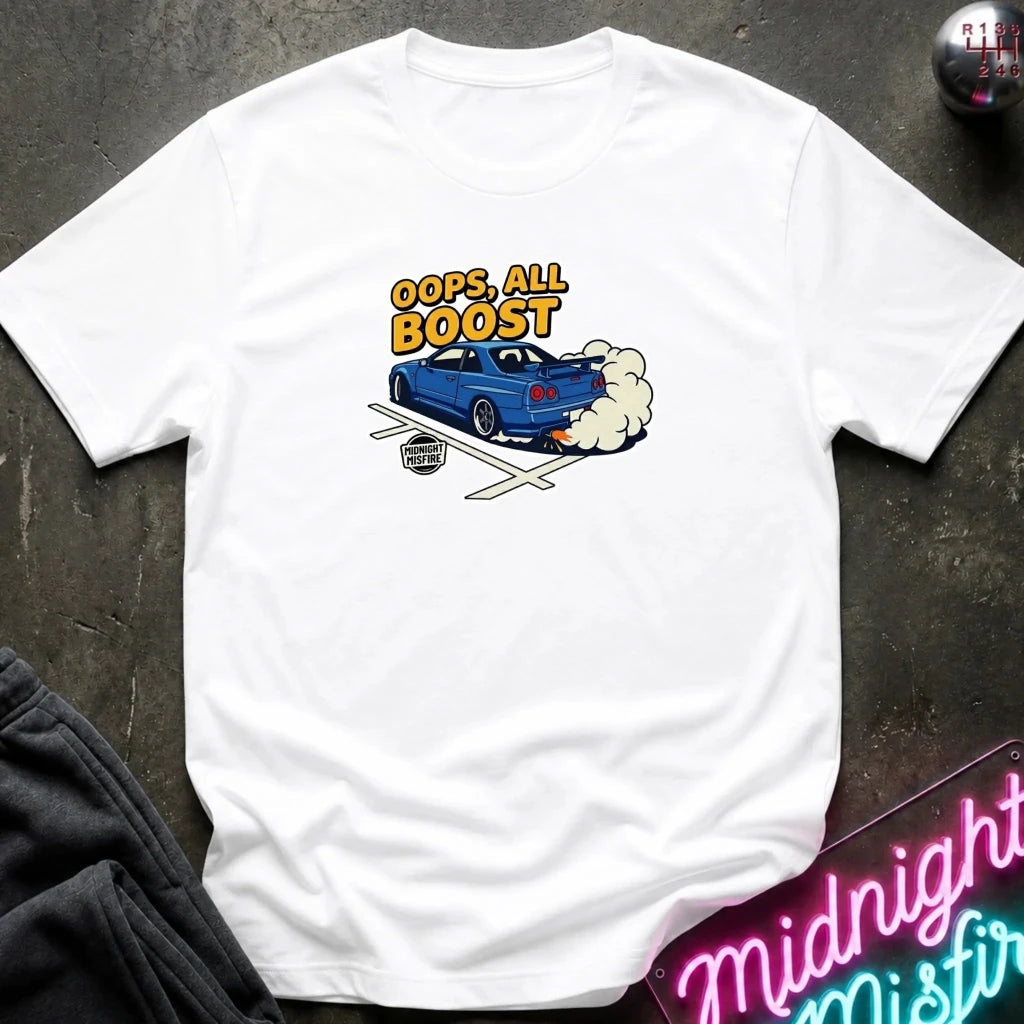 A white short-sleeve t-shirt laid flat on a dark textured surface, featuring a graphic of a blue car with smoke and the text 'OOPS, ALL BOOST' in yellow and orange. 