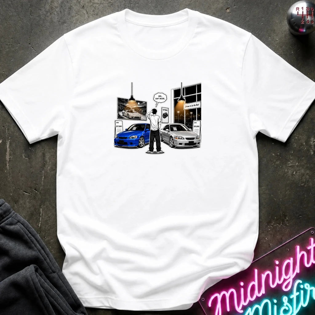 A white short-sleeve t-shirt laid flat on a dark textured surface, featuring a graphic print of a person standing between a blue car and a silver car in front of a storefront.