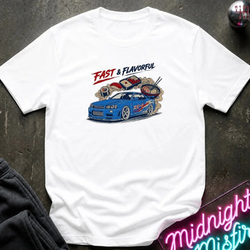 A white short-sleeve graphic T-shirt laid flat on a dark textured surface. The shirt features a colorful print of a blue sports car with ramen noodles and chopsticks, plus the text 'FAST & FLAVORFUL' in red and black.