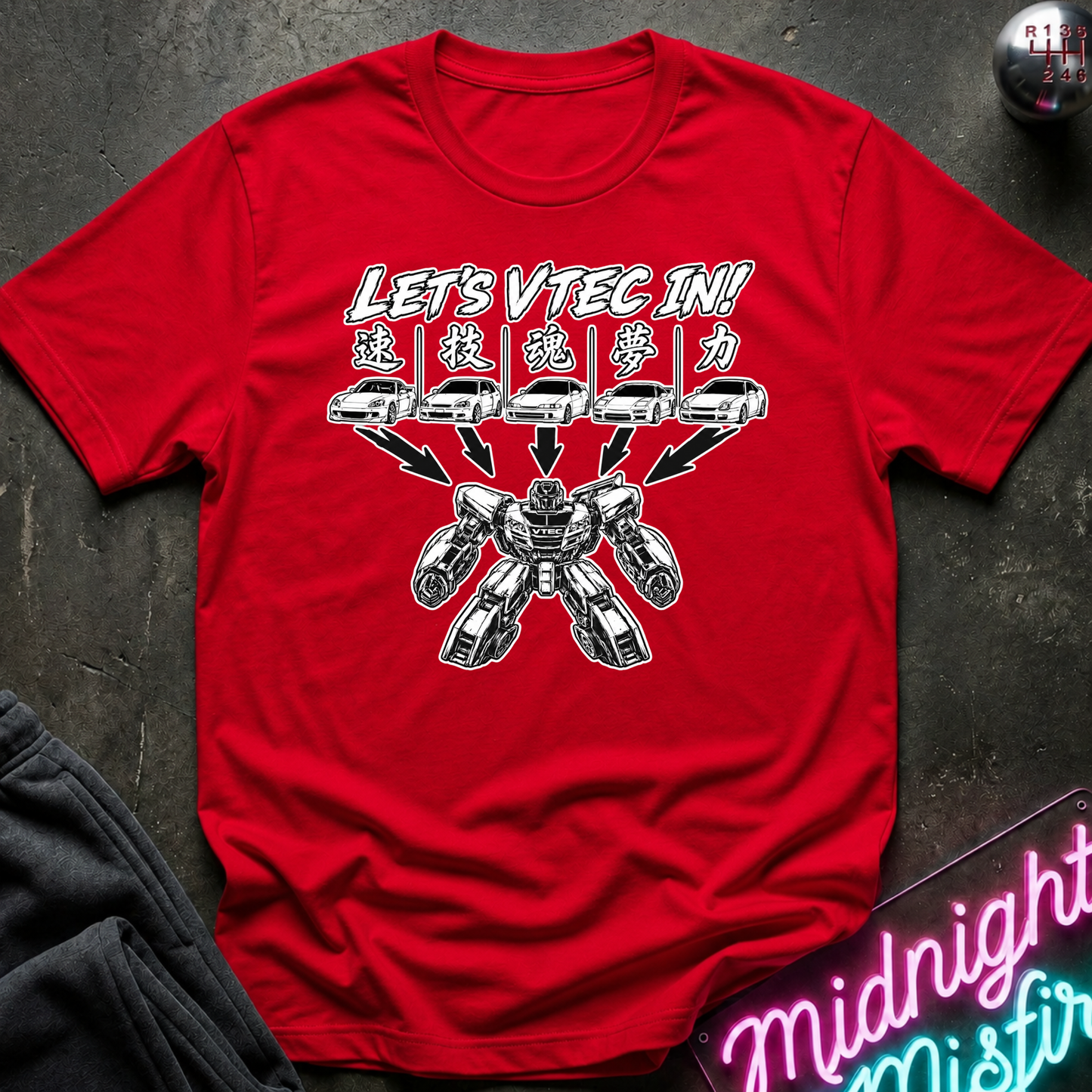 A red short-sleeve graphic T-shirt laid flat on a dark textured surface. The shirt features a white and gray printed design with the text 'LET'S VTEC IN!' and stylized car/robot graphics.