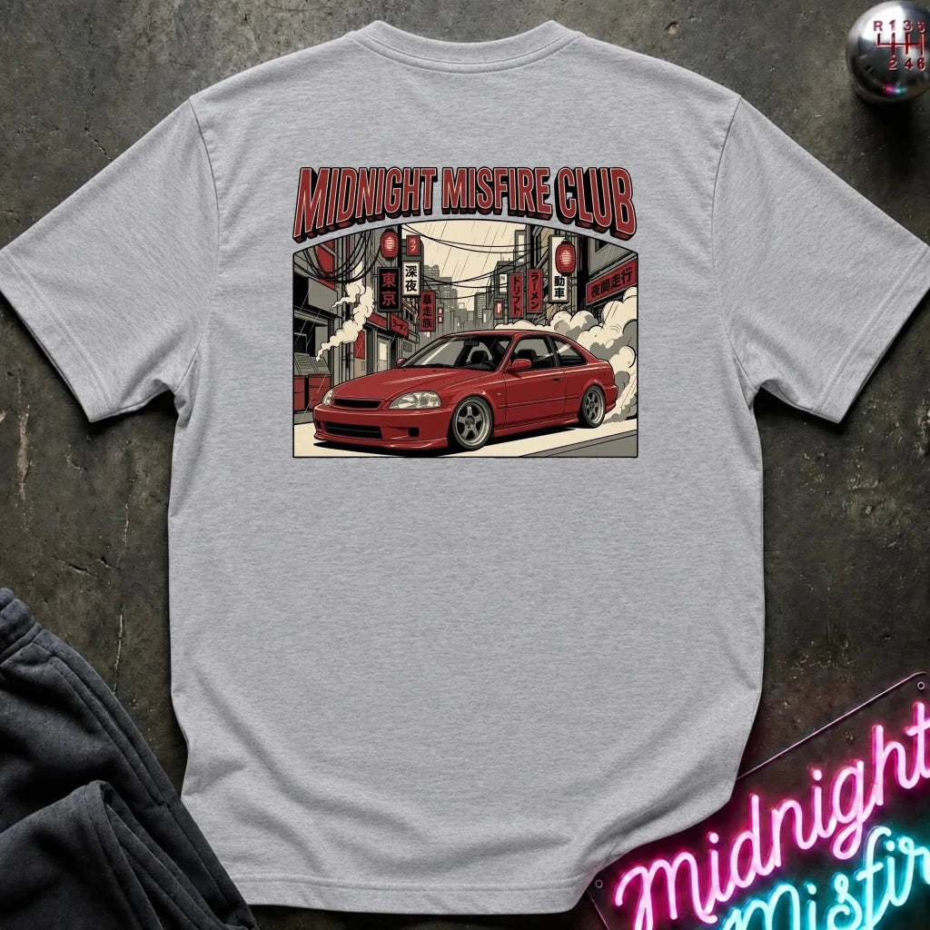A light gray heather crewneck t-shirt laid flat on a dark textured surface, featuring a graphic print of a red sports car in a city street with the text 'MIDNIGHT MISFIRE CLUB'.