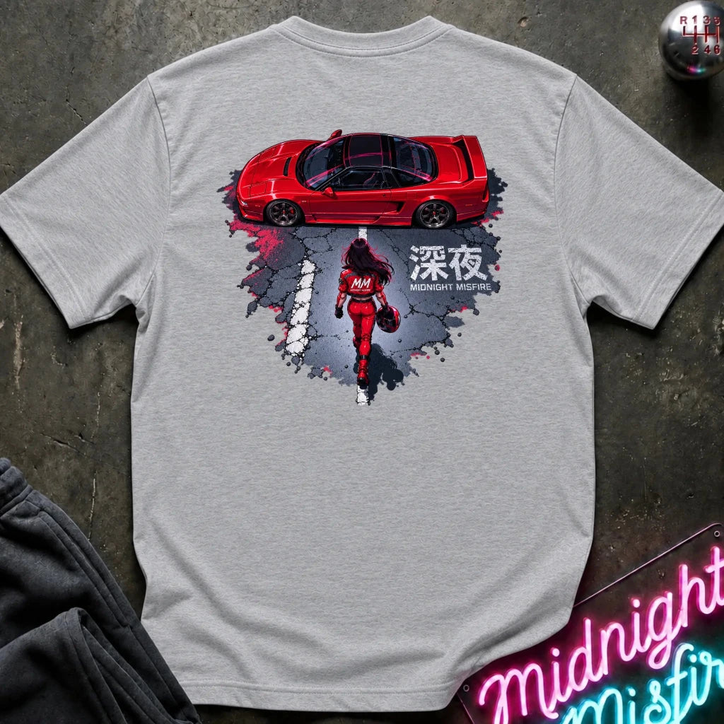 A light gray heather short-sleeve graphic T-shirt laid flat on a dark textured surface. The shirt features a large back print showing a red sports car above a red racer in a splattered gray and black design
