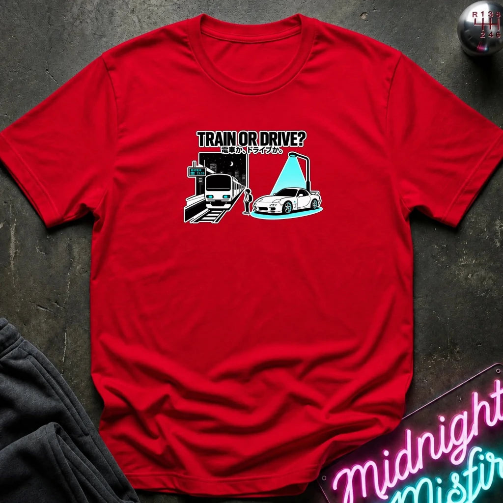 red graphic t-shirt laid flat on a dark textured surface. The graphic features a train and a car with a person.
