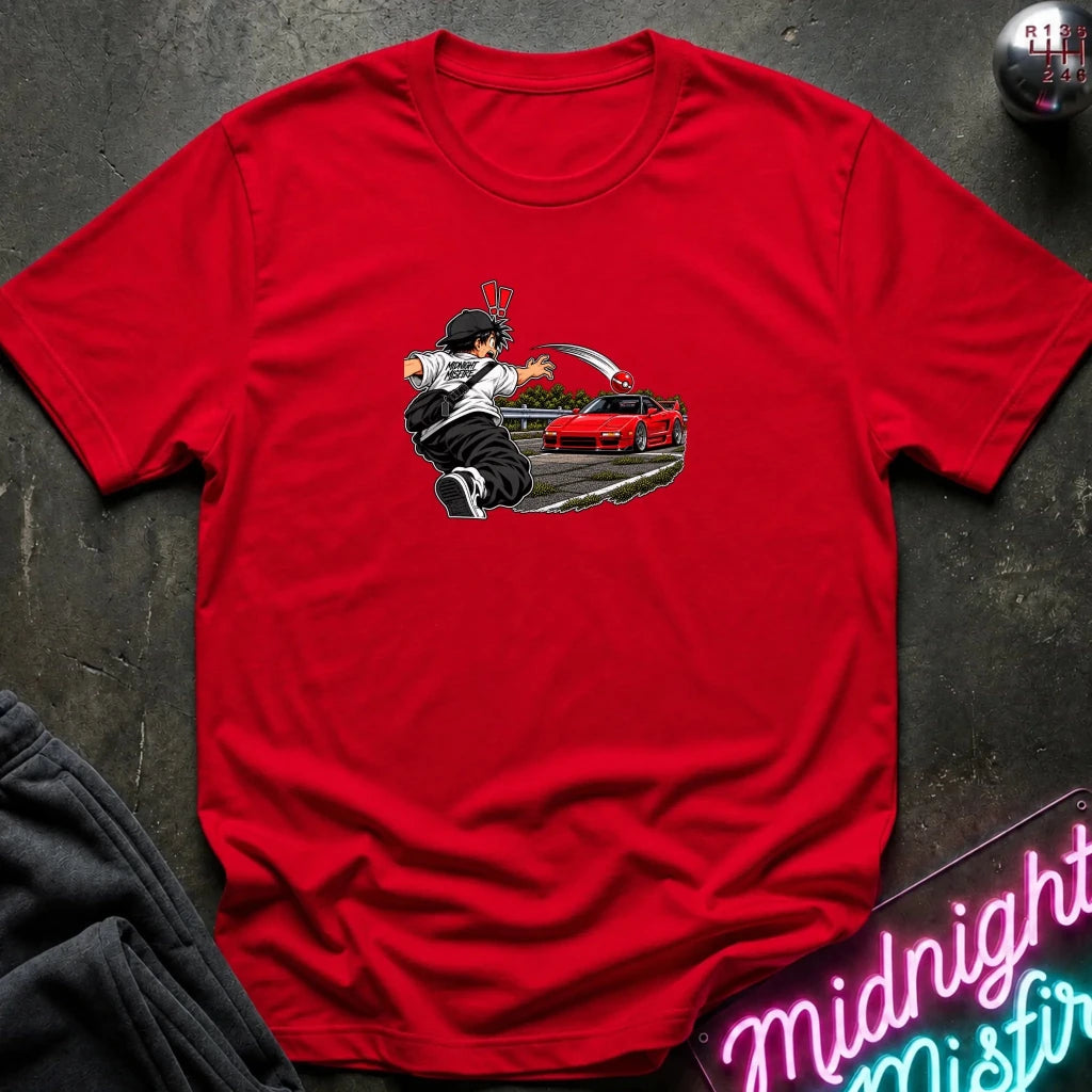 A red short-sleeve crewneck t-shirt laid flat on a dark textured surface. The center of the shirt features a graphic print of an anime character in a black and white outfit with a hat, next to a sports car 