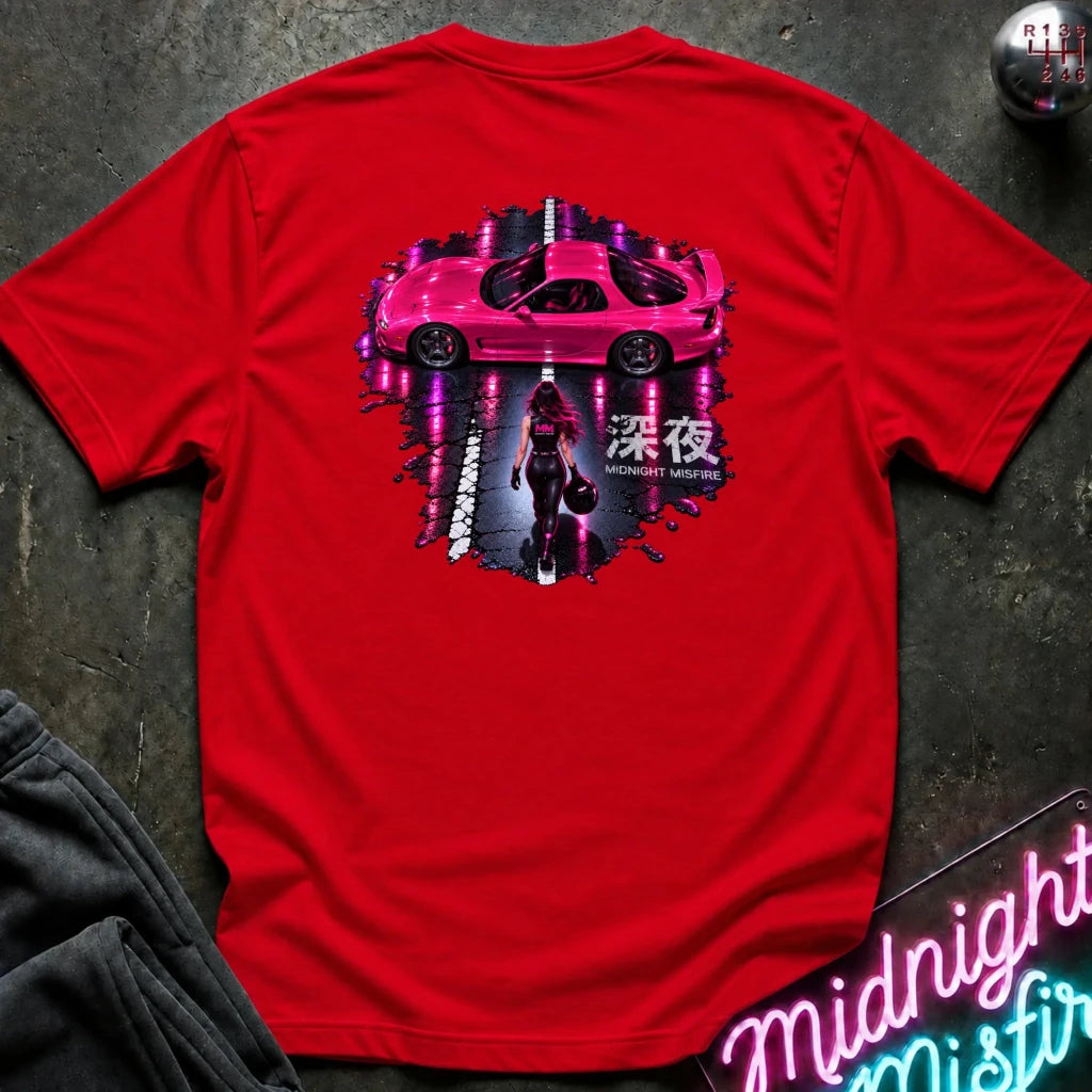 A red short-sleeve t-shirt laid flat on a dark textured surface, featuring a large back graphic of a pink sports car with neon purple reflections, a dark figure, and Japanese text. A neon sign and dark pants are partially visible as props.