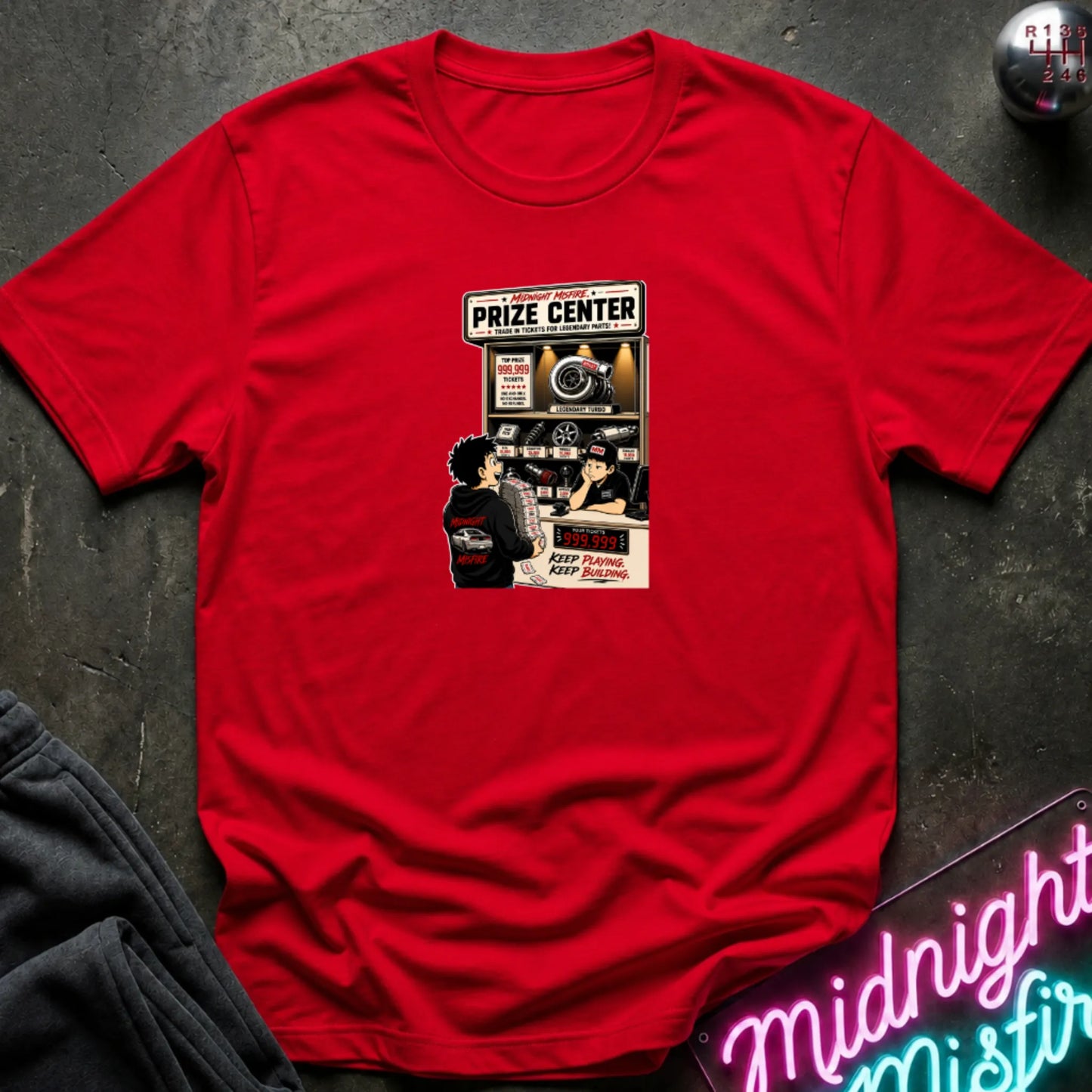 A red short-sleeve crewneck t-shirt laid flat on a dark textured surface, featuring a central graphic print of a prize center for car parts. 