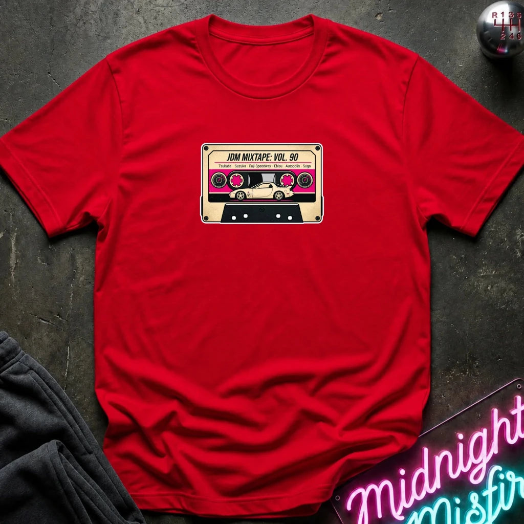 A red crewneck t-shirt laid flat on a dark textured surface, featuring a retro cassette tape graphic on the chest with the text 'JDM MIXTAPE VOL.