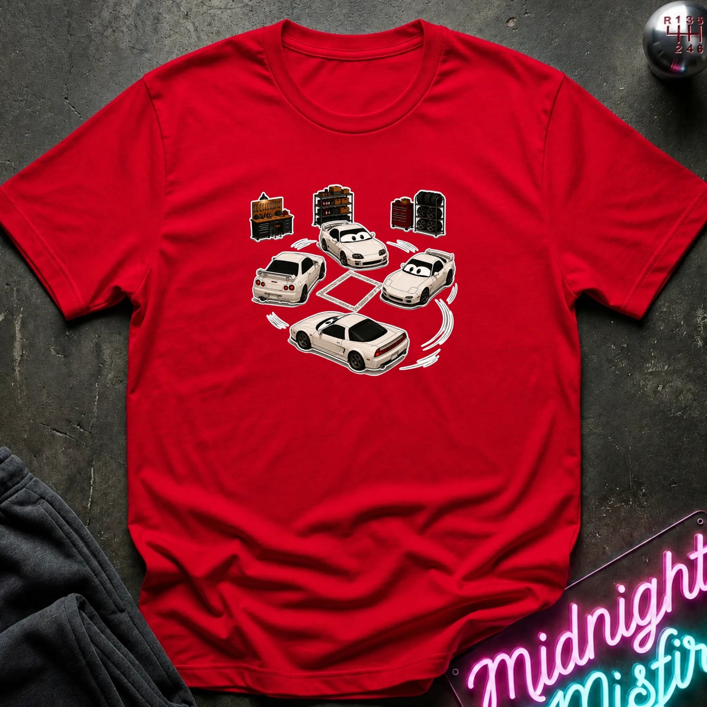 A red short-sleeve t-shirt laid flat on a dark textured surface, featuring a graphic print of several white sports cars arranged in a circle with drift-like tire marks.