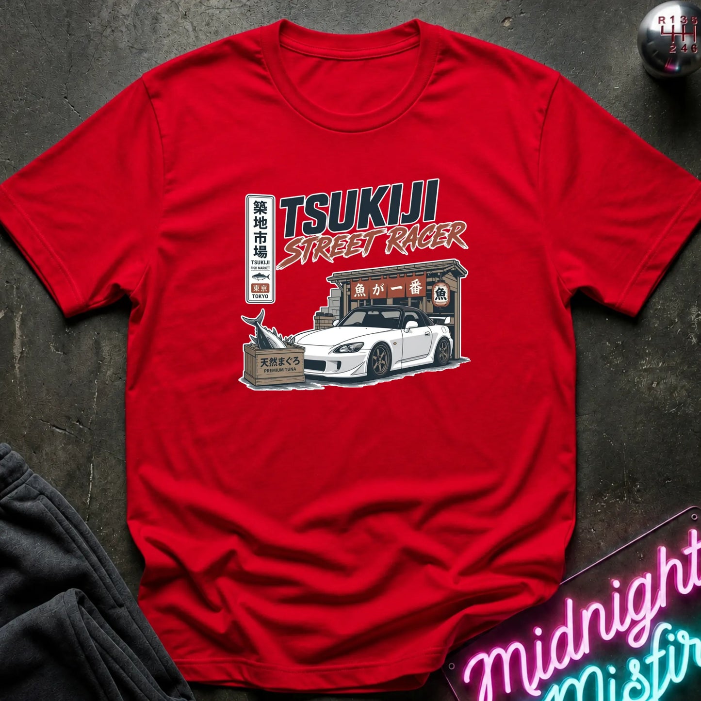 Red short-sleeve graphic T-shirt laid flat on and surrounding an illustration of a white sports car parked outside a fish market.