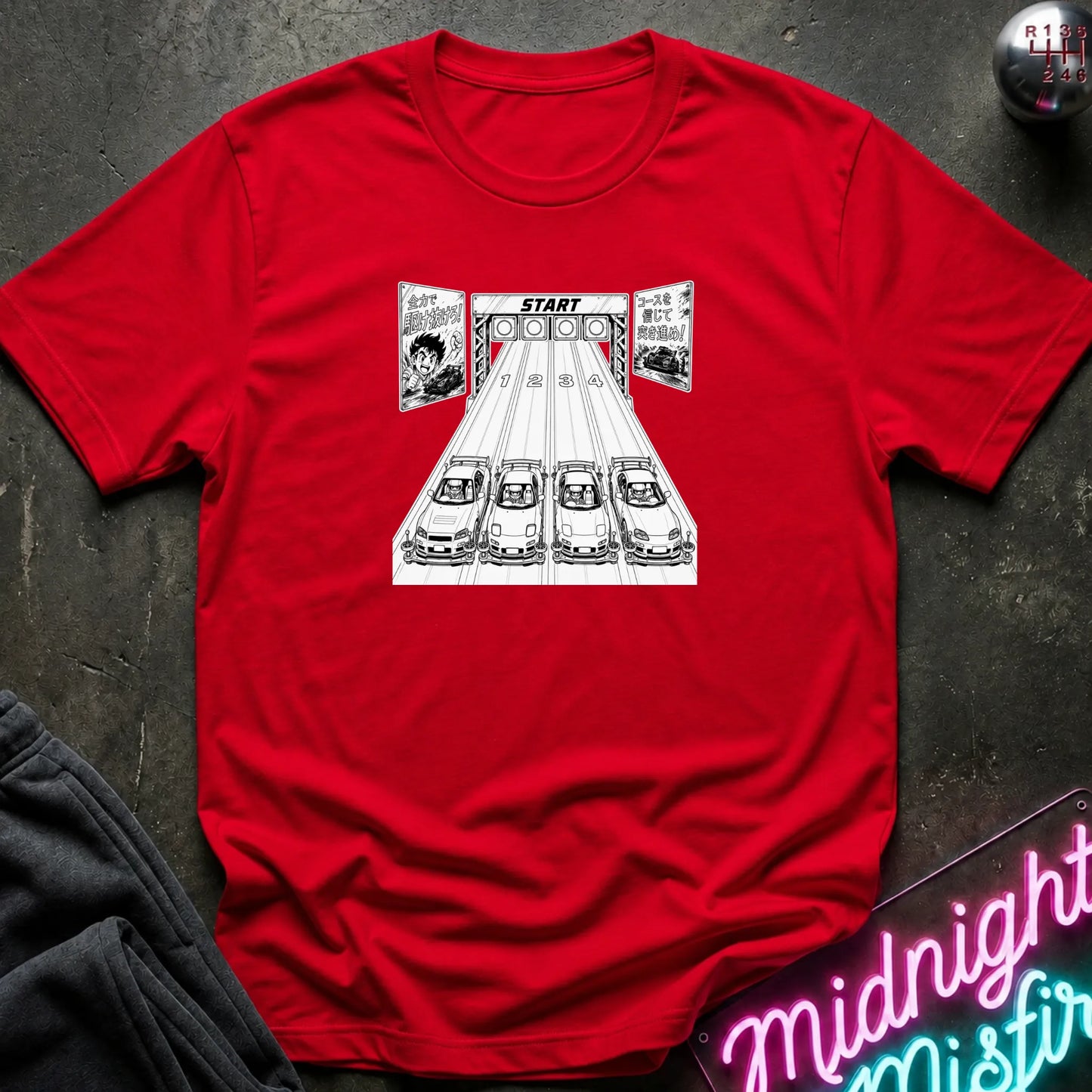 A red short-sleeve t-shirt laid flat on a dark textured surface, featuring a black-and-white graphic of 4 cars lined up at a racing on a track.