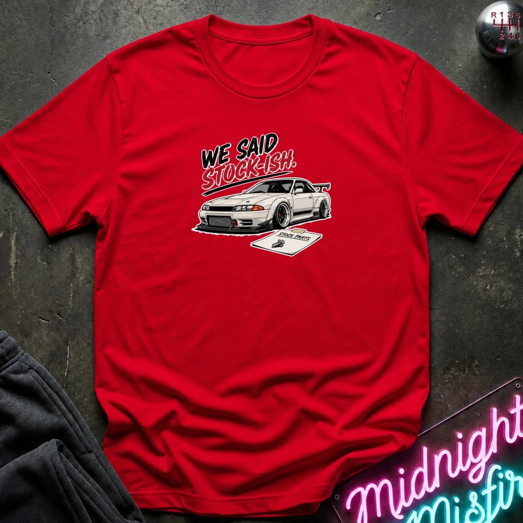 A red short-sleeve graphic T-shirt laid flat on a dark textured surface. The shirt features a white sports car illustration with the text 'WE SAID STOCKISH' above it.