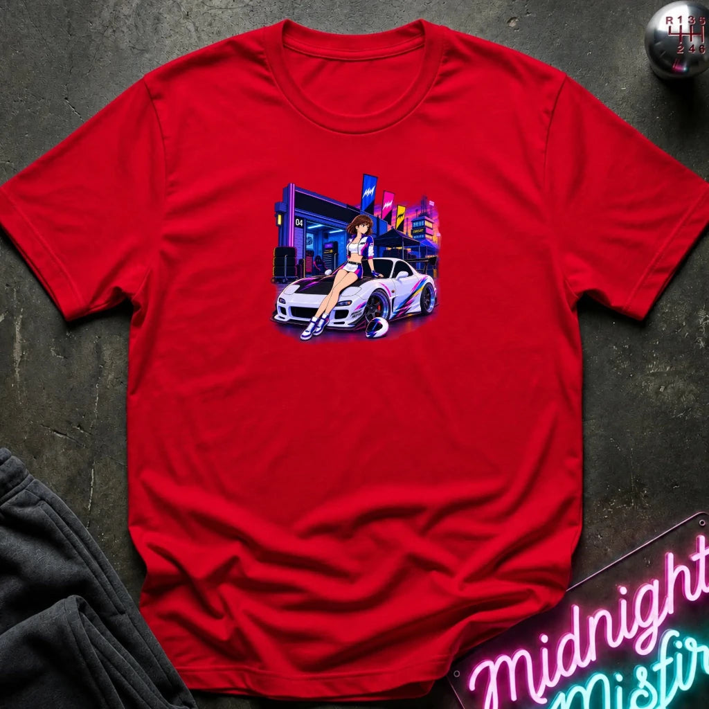 A red  short-sleeve t-shirt laid flat on a dark textured surface, featuring a colorful graphic print of a white sports car and a woman in a neon-lit scene. 