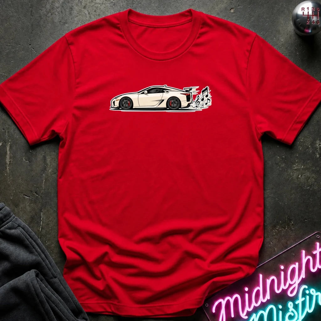 A red short-sleeve crewneck t-shirt featuring a graphic of a white sports car with black wheels and a rear spoiler, laid flat on a dark textured surface with a neon sign and dark pants partially visible.