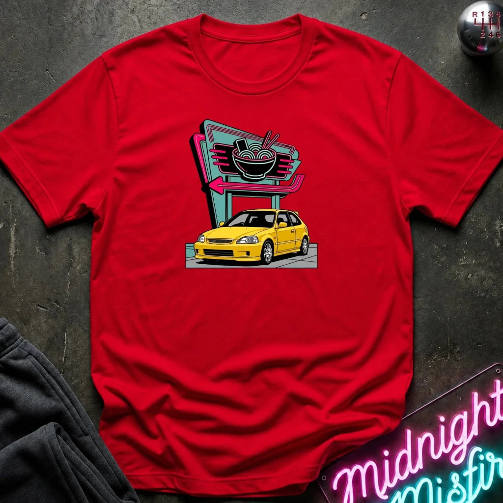 A red short-sleeve t-shirt laid flat on a dark textured surface, featuring a retro-style graphic of a yellow hatchback car parked in front of a neon ramen shop sign. 