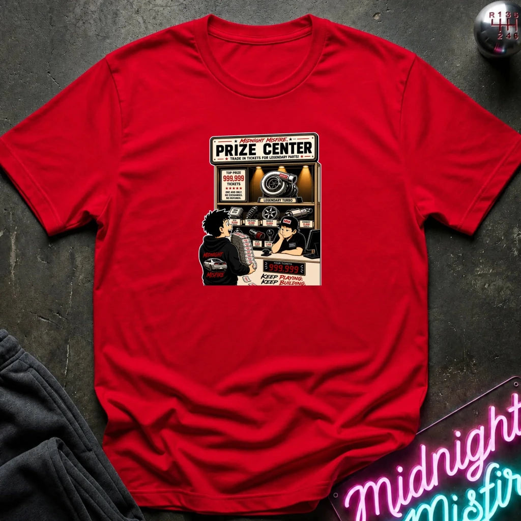 A red short-sleeve crewneck t-shirt with a vintage-style 'Prize Center' concert poster graphic on the chest, displayed flat on a dark textured surface with a neon sign and dark sweatpants nearby.