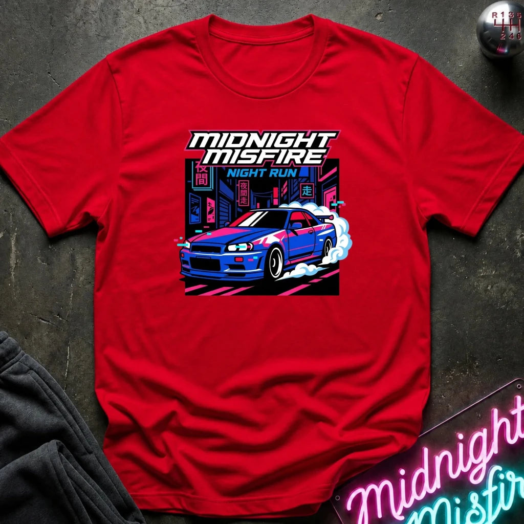 A red short-sleeve graphic T-shirt laid flat on a dark textured surface. The shirt features a colorful front print of a blue and white sports car with smoke effects and the text 'MIDNIGHT MISFIRE' and 'NIGHT RUN'.