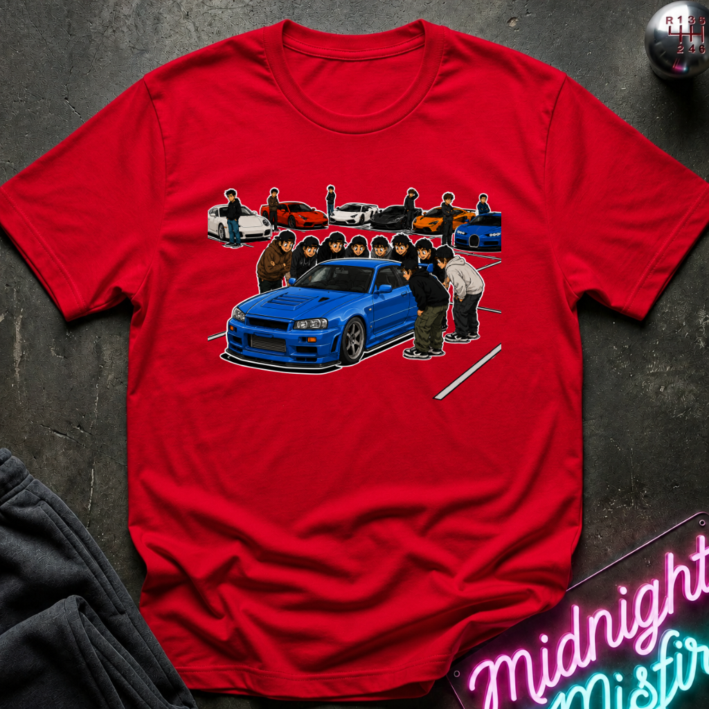 A red short-sleeve crewneck t-shirt featuring a graphic print of a blue sports car and anime characters, laid flat on a dark textured surface with a neon sign and dark sweatpants partially visible.