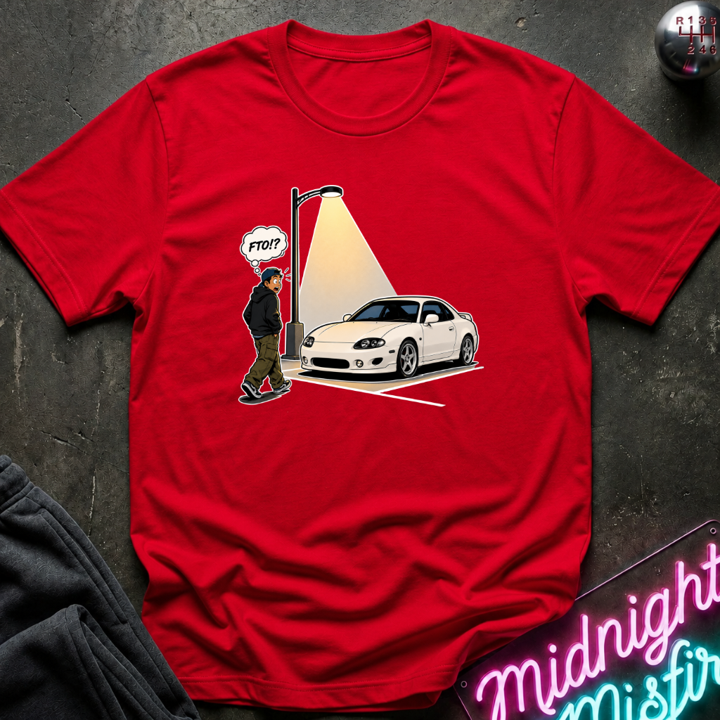 A red short-sleeve graphic t-shirt laid flat on a dark textured surface. The graphic shows a white sports car under a streetlamp with a spotlight effect, alongside a walking figure.