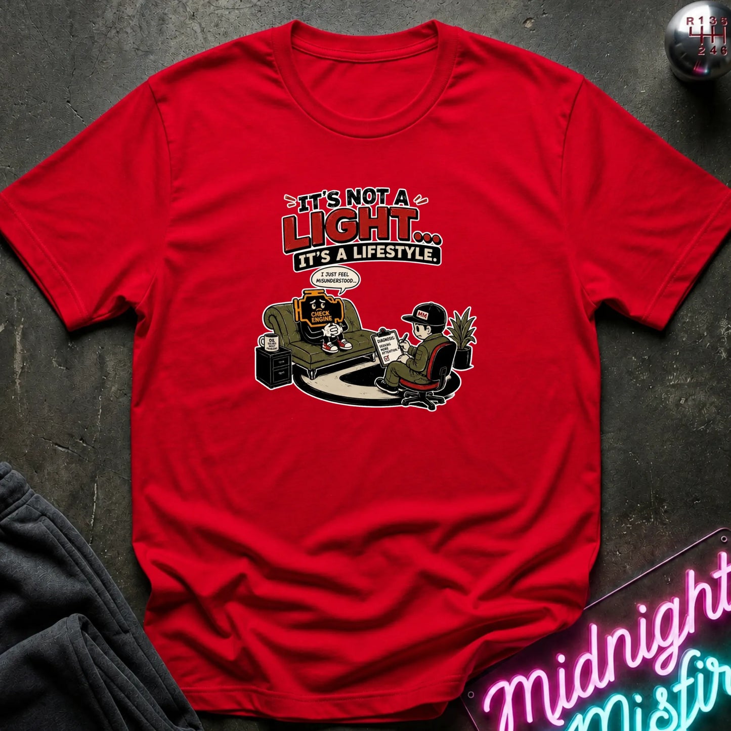A red short-sleeve graphic t-shirt laid flat on a dark textured surface. The graphic features the text 'IT'S NOT A LIGHT.