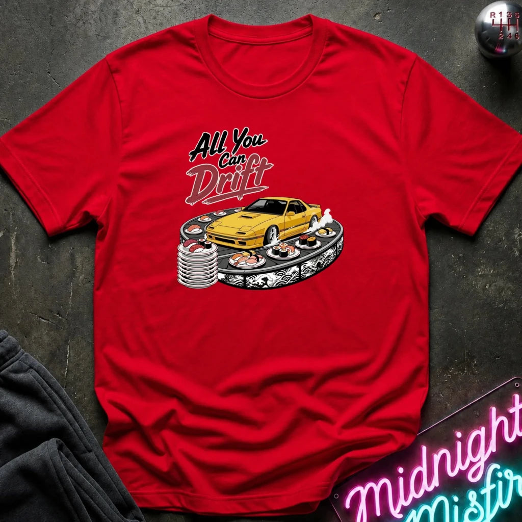 A red short-sleeve graphic T-shirt laid flat on a dark textured surface. The shirt features a printed design with the text 'All You Can Drift' above a yellow sports car surrounded by sushi and a stack of coins.