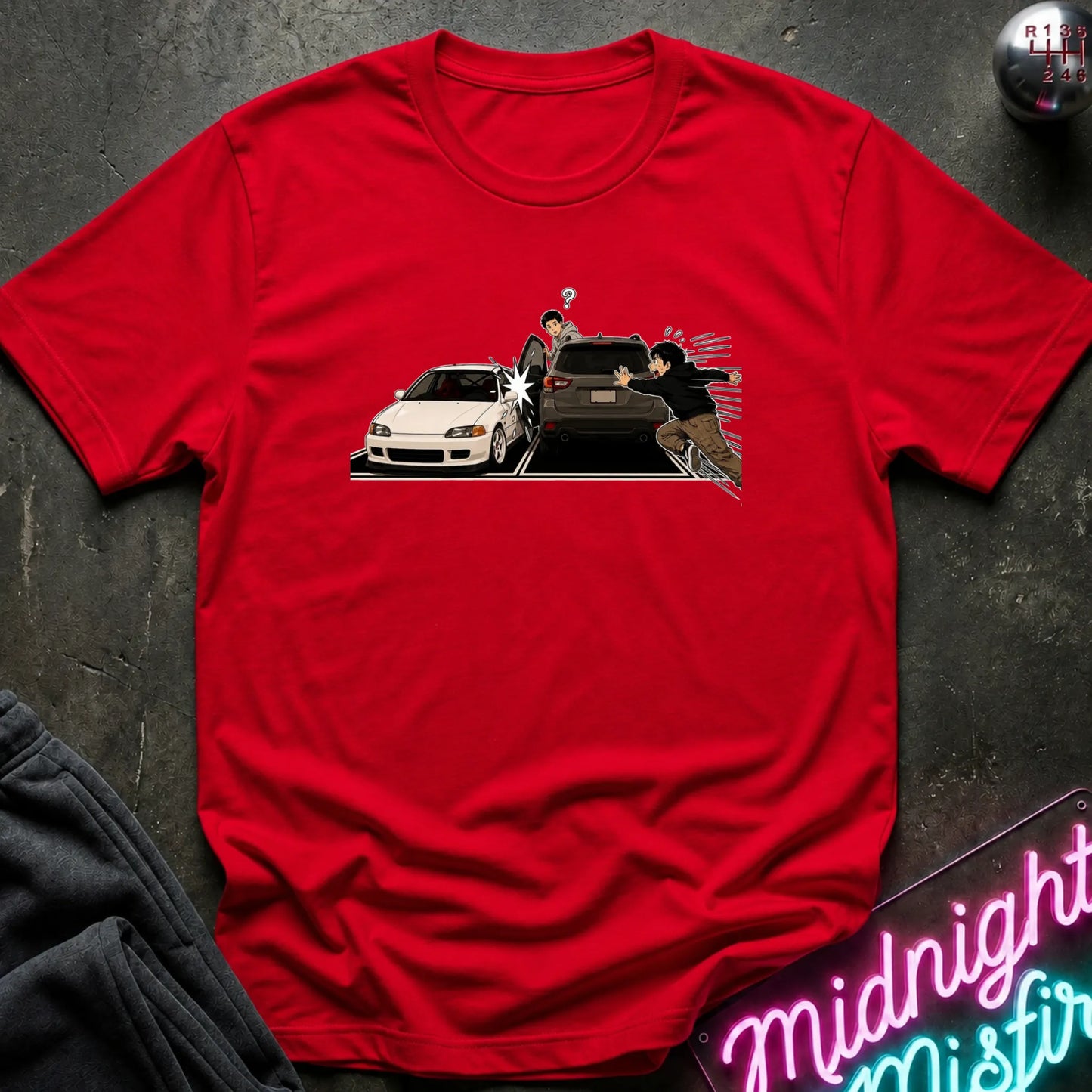 A red short-sleeve crewneck t-shirt laid flat on a dark textured surface, featuring a graphic print of a white sports car and a black SUV with characters.