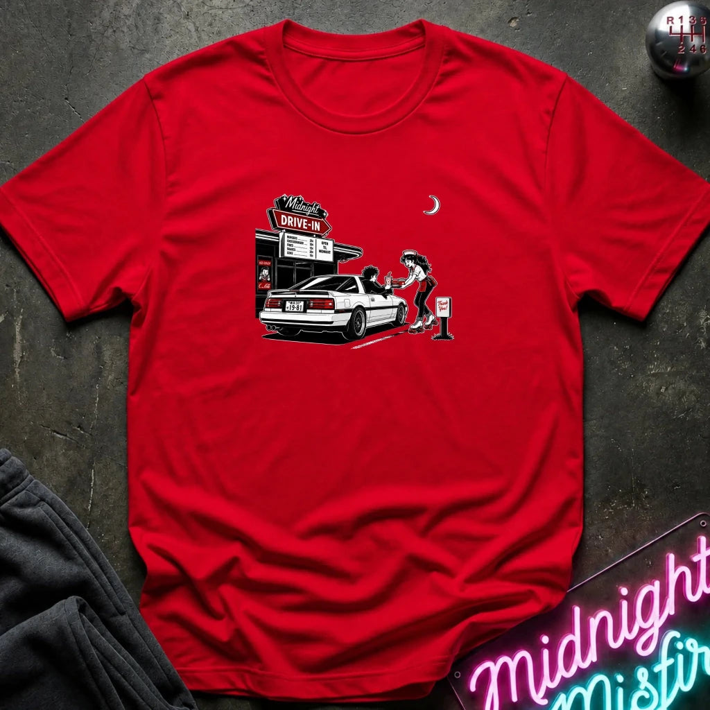 A red short-sleeve t-shirt laid flat on a dark textured surface, featuring a graphic print of a woman pumping gas at a drive-in station next to a white car. 