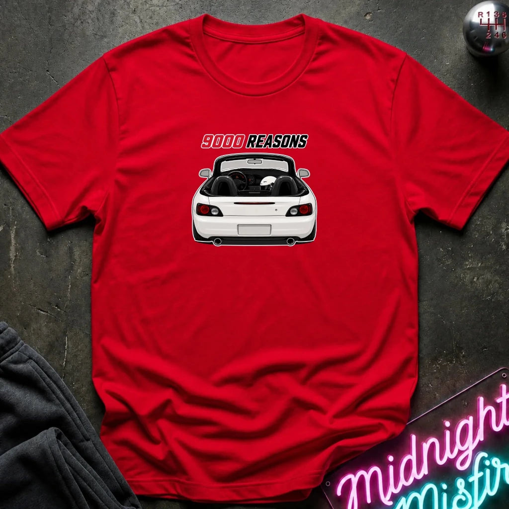 A red short-sleeve crewneck t-shirt laid flat on a dark textured surface. The shirt features a graphic print of a white convertible car with the text '9000 REASONS' above it.