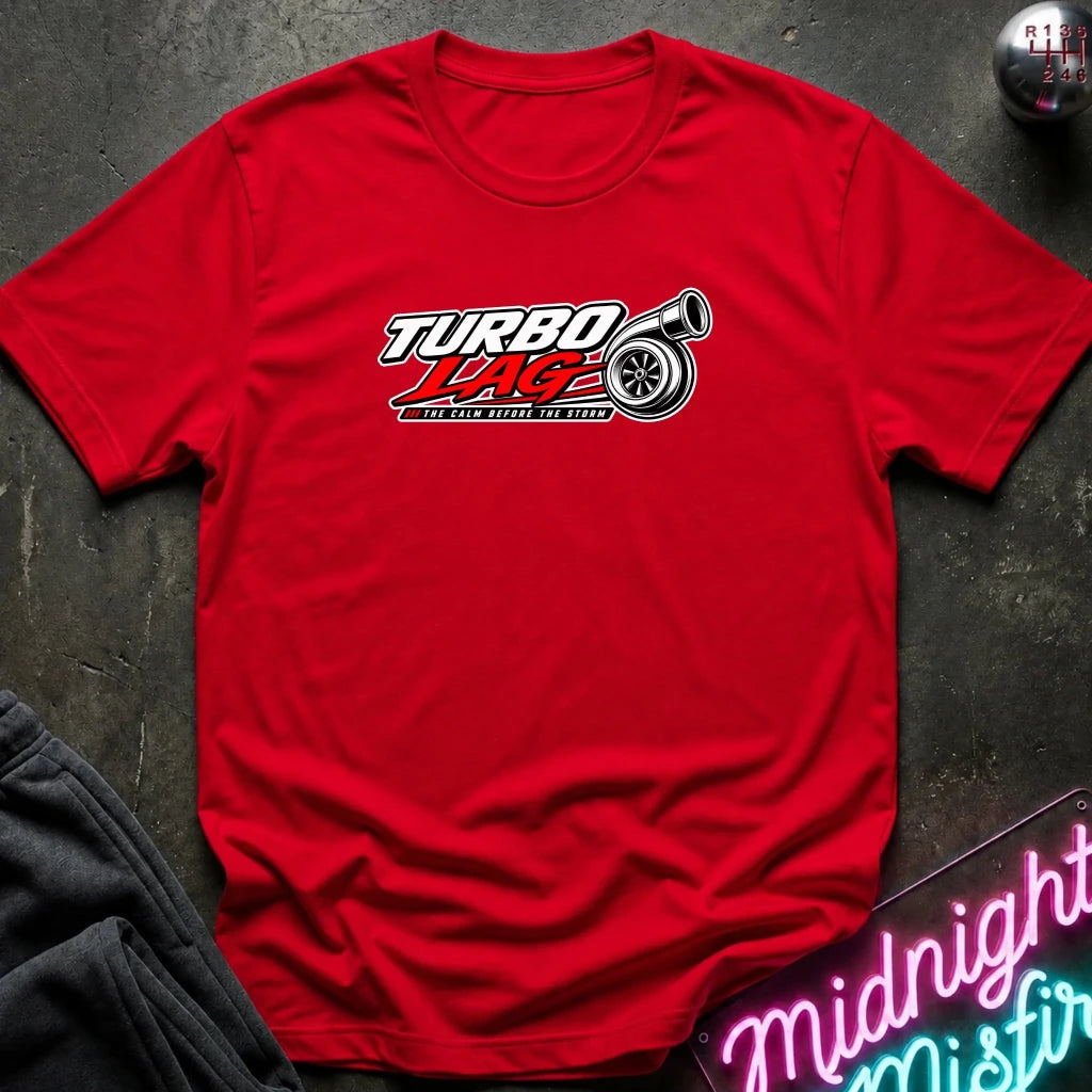 A red short-sleeve t-shirt with a 'Turbo Race' graphic on the chest, laid flat on a dark textured surface with a gear and neon sign props.