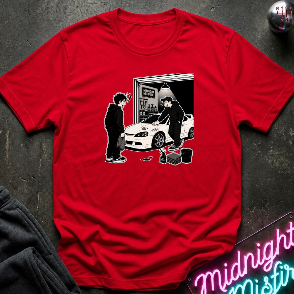 A red short-sleeve crewneck t-shirt with a black and white graphic print of a person and car next to a garage, laid flat on a dark textured surface with a neon sign and dark sweatpants in the background.
