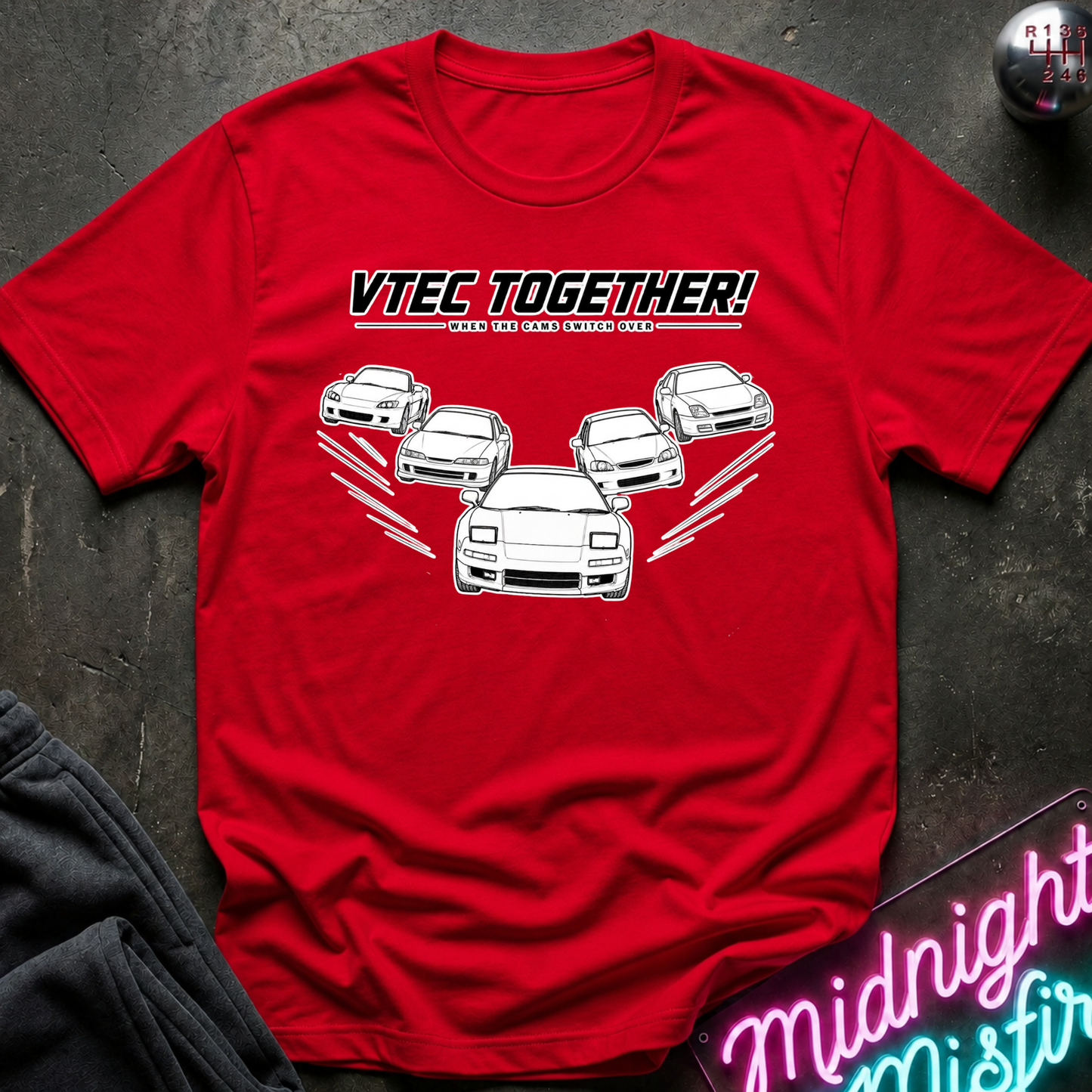 A red short-sleeve graphic T-shirt laid flat on a dark textured surface. The shirt features the text 'VTEC TOGETHER!' with smaller text below and a white line drawing of several cars arranged in a racing formation.