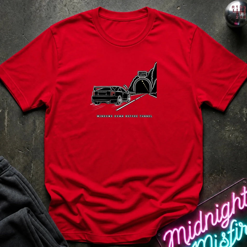 A red short-sleeve t-shirt laid flat on a dark textured surface, featuring a black graphic of a classic car in a tunnel with the text.