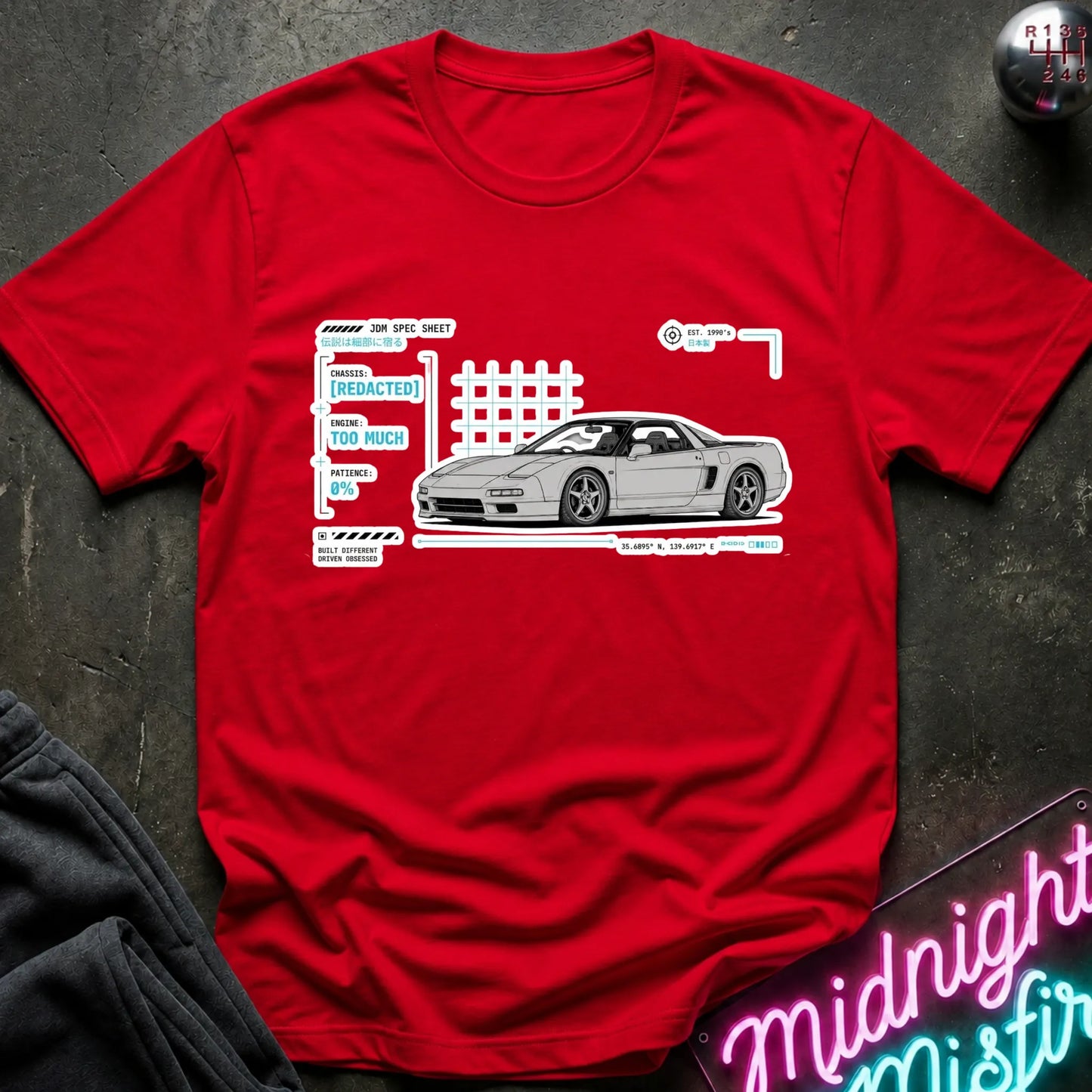 A red short-sleeve graphic T-shirt laid flat on a dark textured surface. The shirt features a white and gray print of a sports car with technical-style labels and a grid graphic.