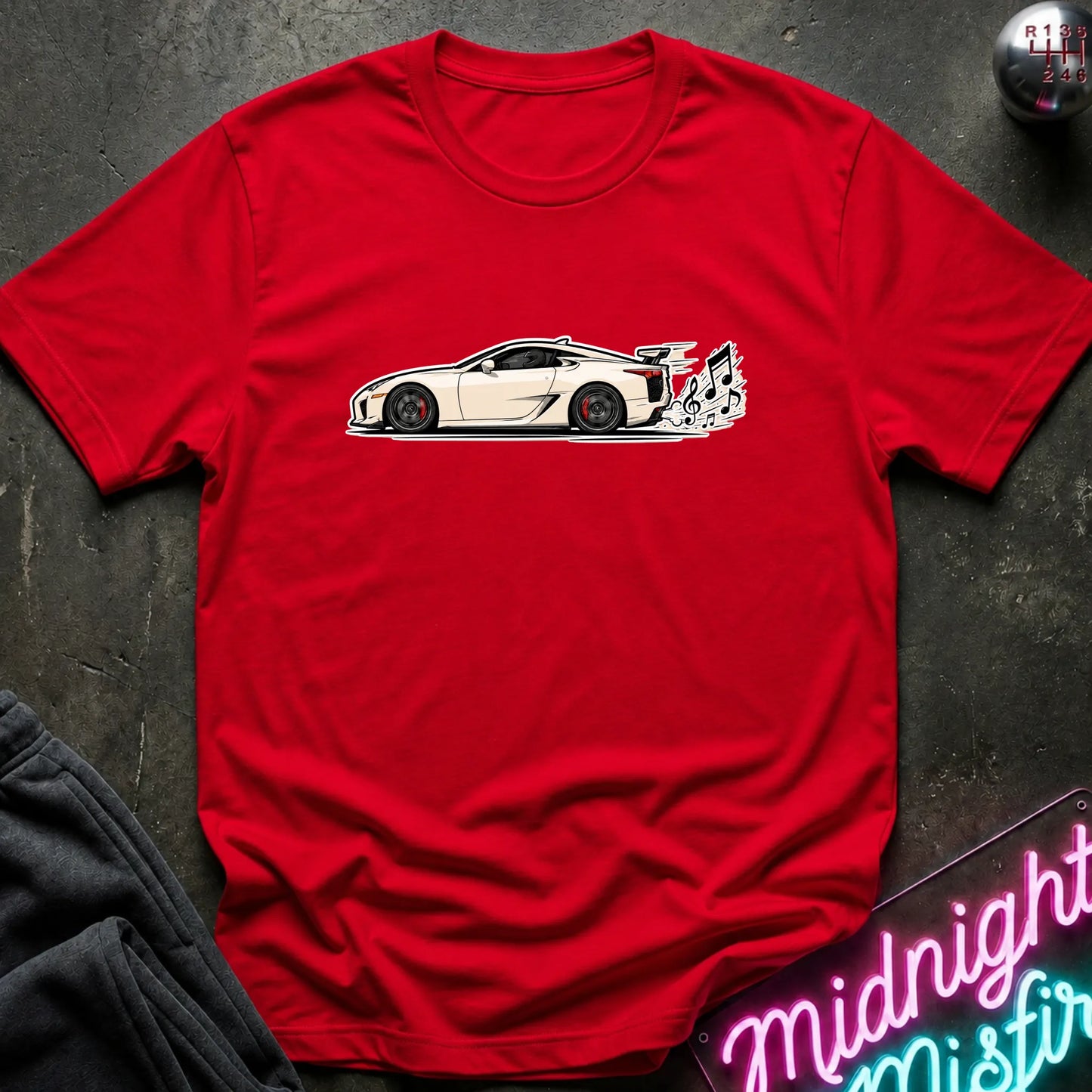 A red short-sleeve t-shirt laid flat on a dark textured surface, featuring a graphic print of a white sports car with a music note coming from exhaust.