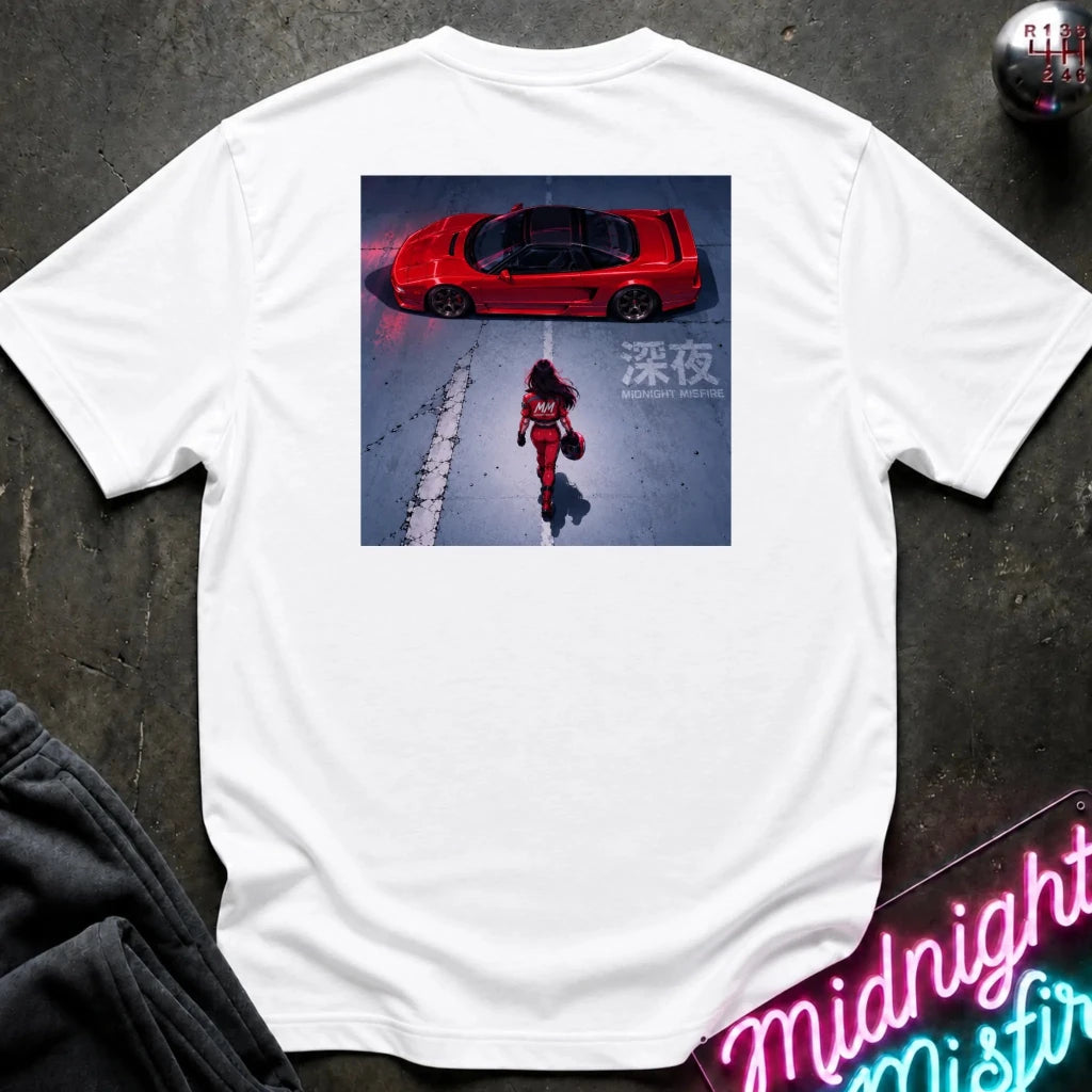 A white short-sleeve t-shirt laid flat on a dark textured surface, featuring a rectangular graphic print on the back with a red sports car and a figure in a red outfit on a snowy ground. A neon sign and dark clothing are partially visible around the edges.