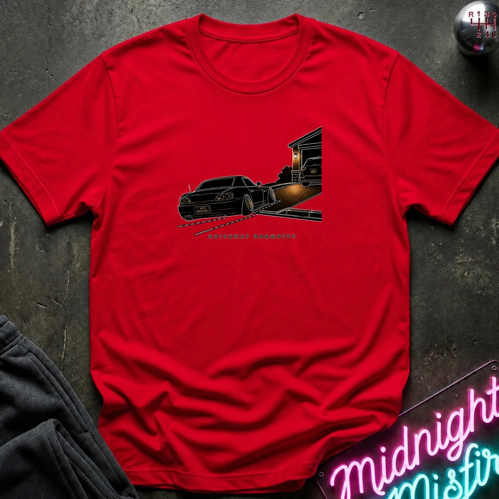 A red short-sleeve t-shirt laid flat on a dark textured surface, featuring a graphic print of a black classic car going up the driveway.