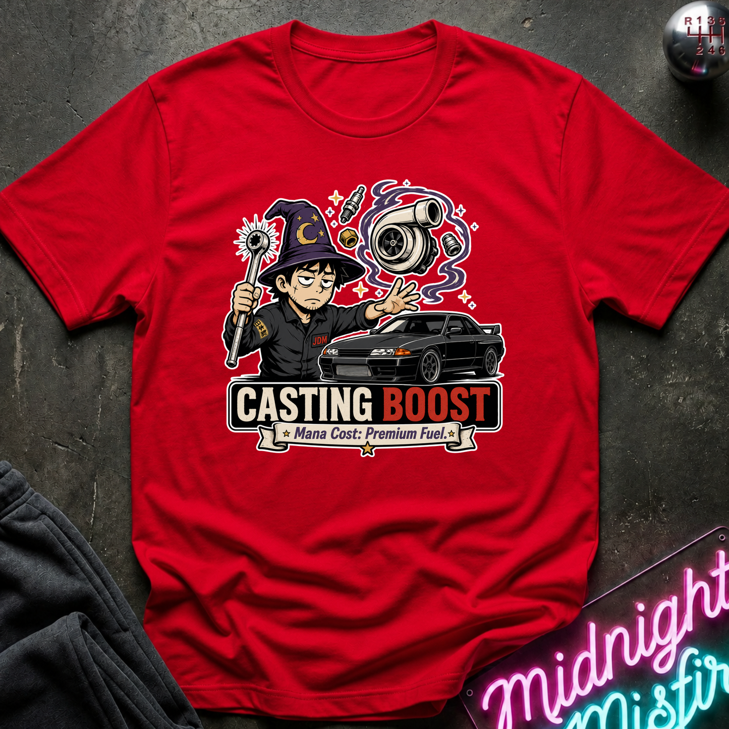 A red short-sleeve graphic T-shirt laid flat on a dark textured surface. The shirt features a colorful cartoon illustration of a wizard character, a black car, and the text 'CASTING BOOST' with smaller text below.