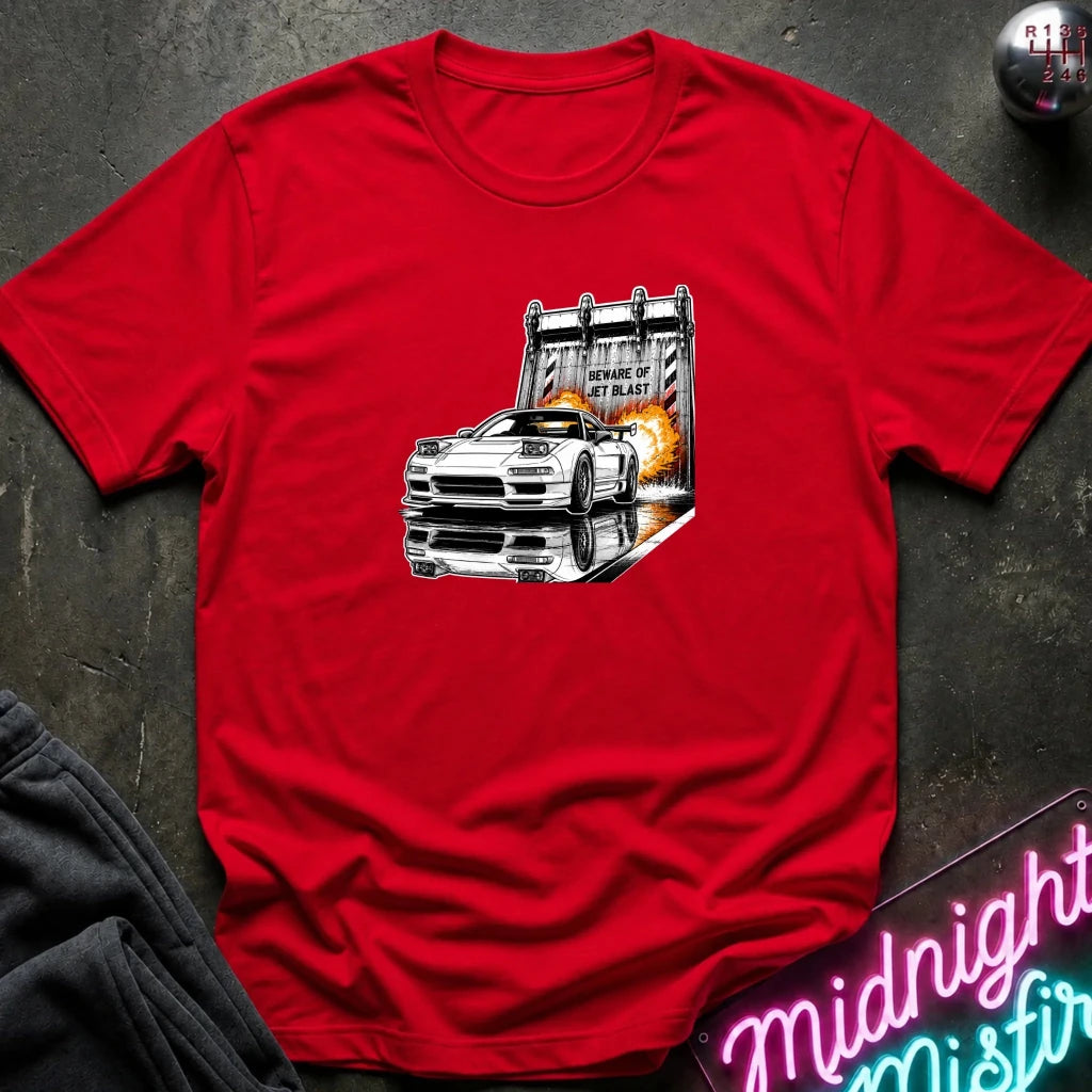 A red  short-sleeve t-shirt laid flat on a dark textured surface, featuring a graphic print of a white sports car in front of a blast off area.