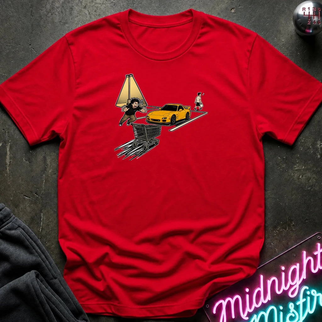A red short-sleeve crewneck t-shirt laid flat on a dark textured surface. The center of the shirt features a graphic print depicting a cartoon raccoon pushing a shopping cart next to a yellow sports car, with a small figure walking in the background.