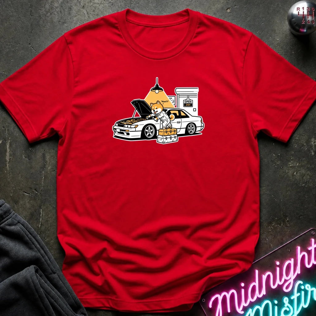 red graphic t-shirt laid flat on a dark textured surface. The graphic features a dog fixing a car.