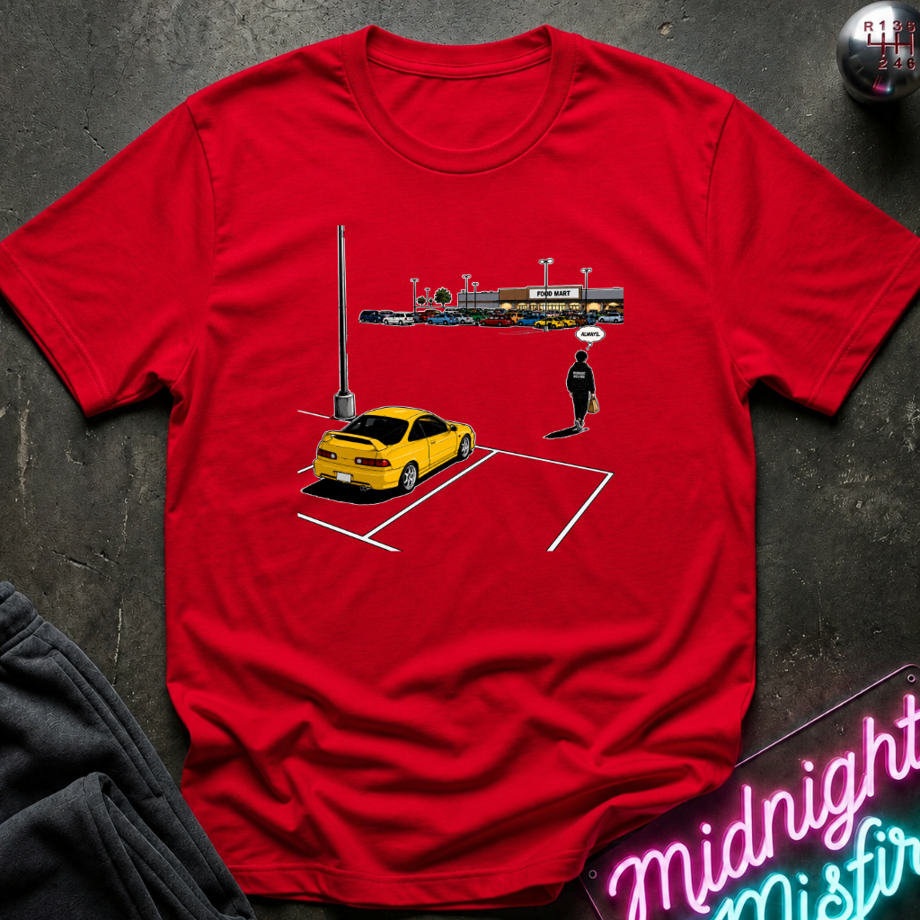 A red short-sleeve graphic t-shirt laid flat on a dark textured surface. The graphic shows a yellow sports car parked in a white-lined parking space with a small figure standing nearby and a row of colorful storefront signs above.