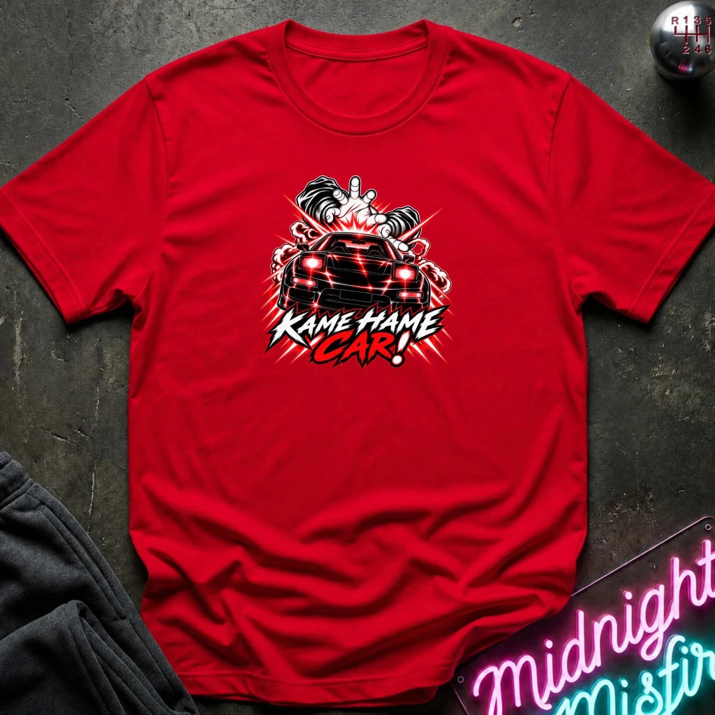 A red short-sleeve graphic t-shirt laid flat on a dark textured surface. The shirt features a red, white, and black graphic of a car with the text 'KAME HAME CAR!' in stylized lettering.