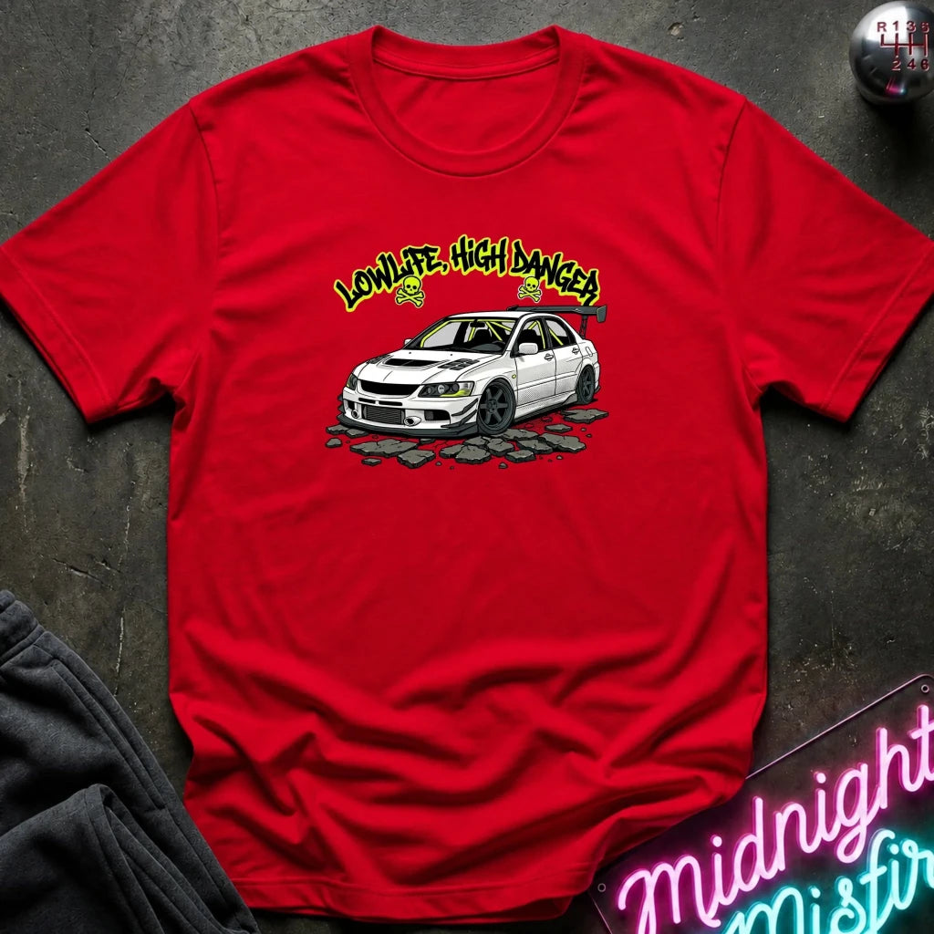 A red short-sleeve graphic t-shirt laid flat on a dark textured surface. The graphic features a white Mitsubishi Lancer Evolution sedan with the text 'LOWLIFE, HIGH DANGER' in yellow above it.