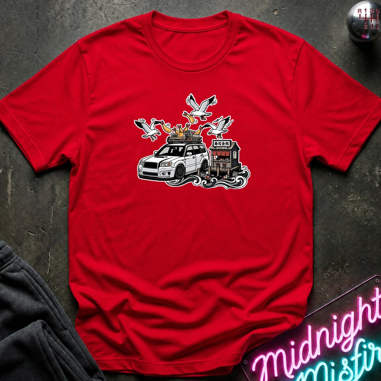 A red short-sleeve crewneck t-shirt with a graphic print of a white SUV, seagulls, laid flat on a dark textured surface.