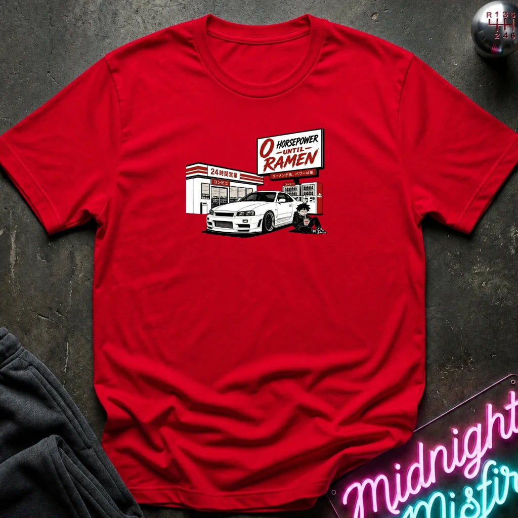 A red crewneck t-shirt laid flat on a dark textured surface, featuring a graphic print of a white sports car parked in front of a konbini.