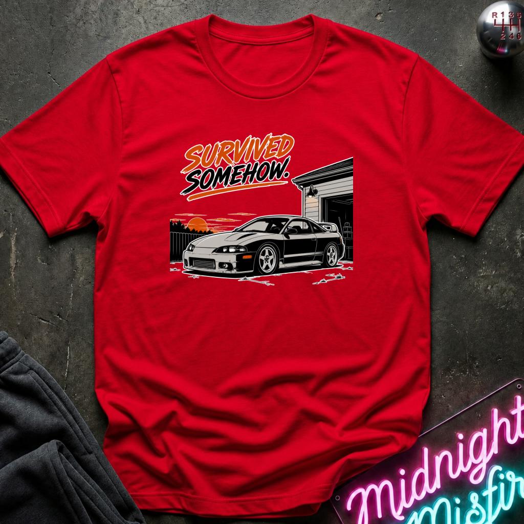A red short-sleeve graphic t-shirt laid flat on a dark textured surface. The graphic features the text 'SURVIVED SOMEHOW.