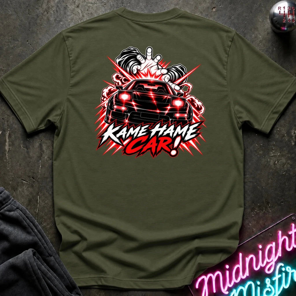 An olive green short-sleeve t-shirt laid flat on a dark textured surface, featuring a large graphic print on the back with a black car, red and white flames, and the text 'KAME HAME CAR!'.