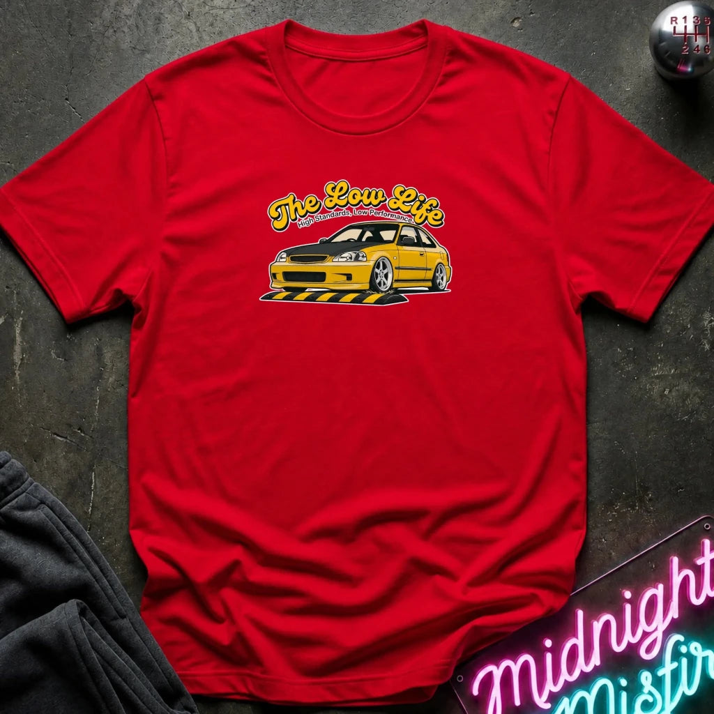 red graphic t-shirt laid flat on a dark textured surface. The shirt features a yellow and white graphic of a low-profile station wagon with the text 'The Low Life' in yellow script.