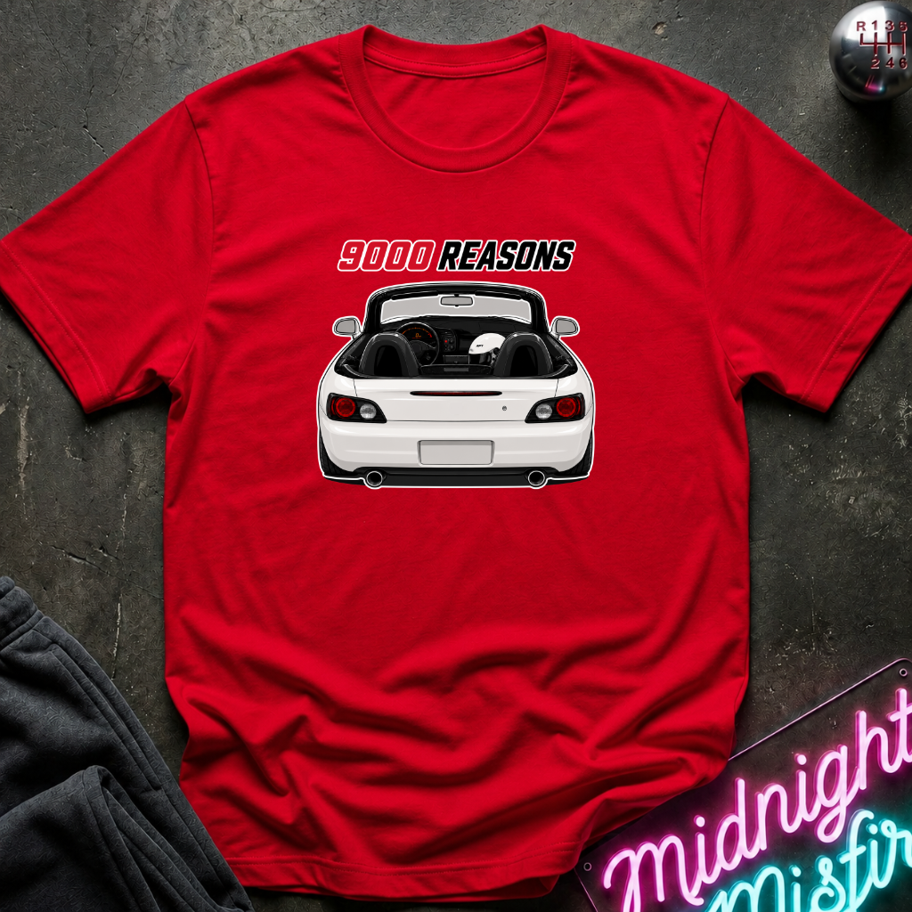 A red short-sleeve t-shirt laid flat on a dark textured surface, featuring a graphic of a white convertible car with the text '9000 REASONS' above it. A neon sign and dark clothing are partially visible around the edges as styling props.