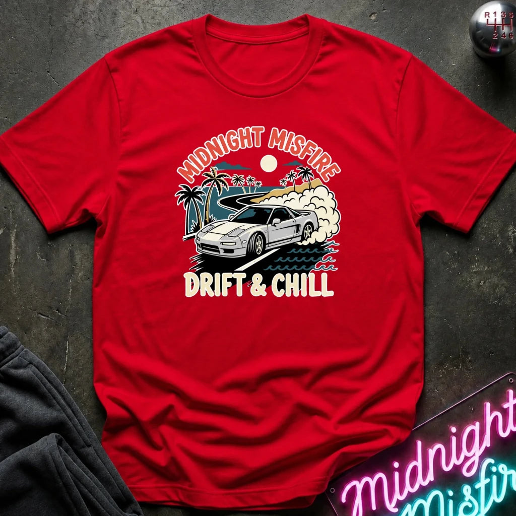 A red short-sleeve graphic T-shirt laid flat on a dark textured surface. The front print shows a white sports car, palm trees, waves, and the text 'MIDNIGHT MISFIRE' and 'DRIFT & CHILL' in cream and blue tones.