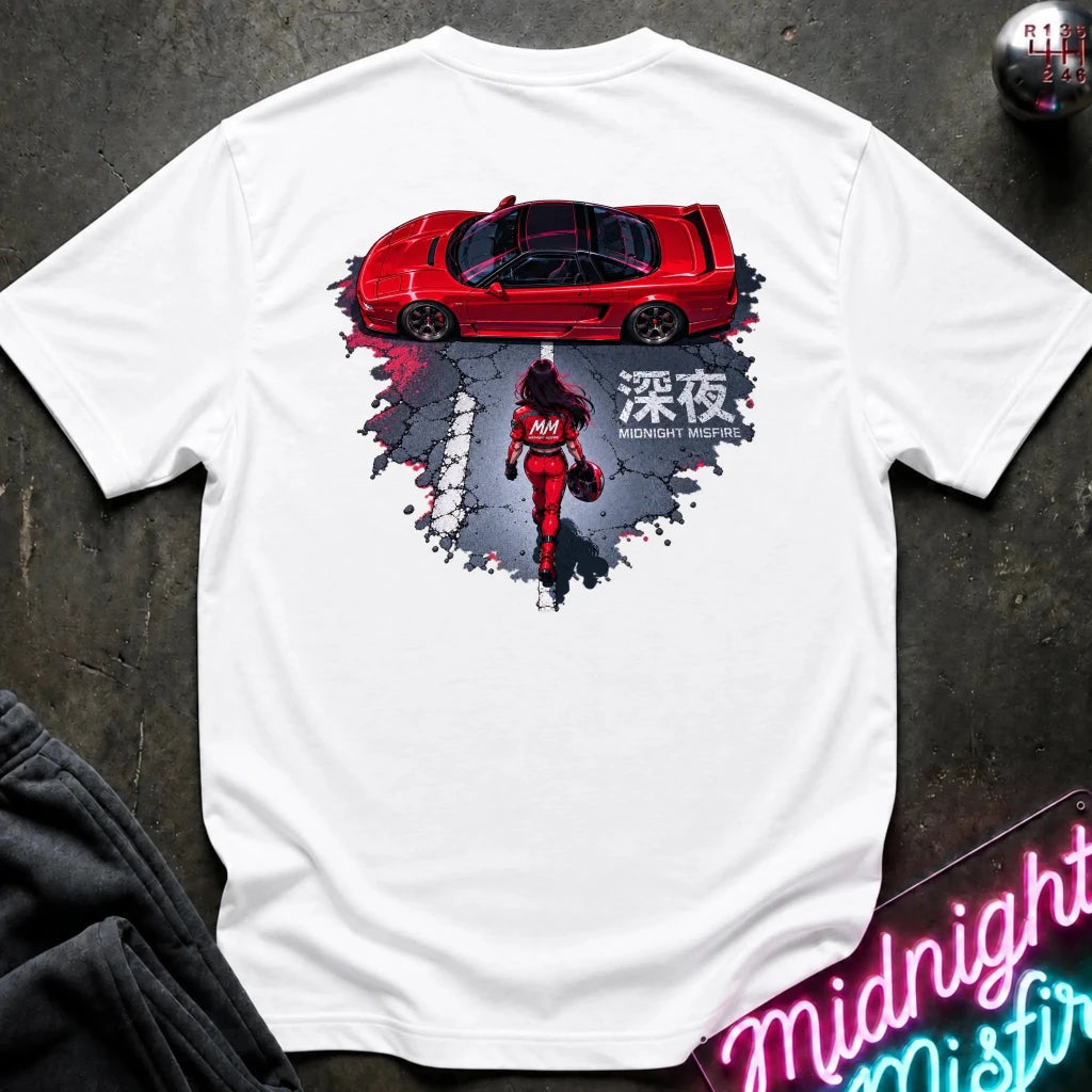 A white short-sleeve graphic T-shirt laid flat on a dark textured surface. The shirt features a large back print showing a red sports car above a red racer in a splattered gray and black design